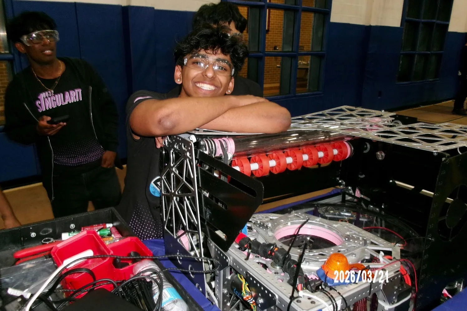 A student hugging the bare robot chassis in the gym